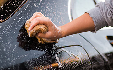 A close up of a person wiping down a car with a soapy sponge